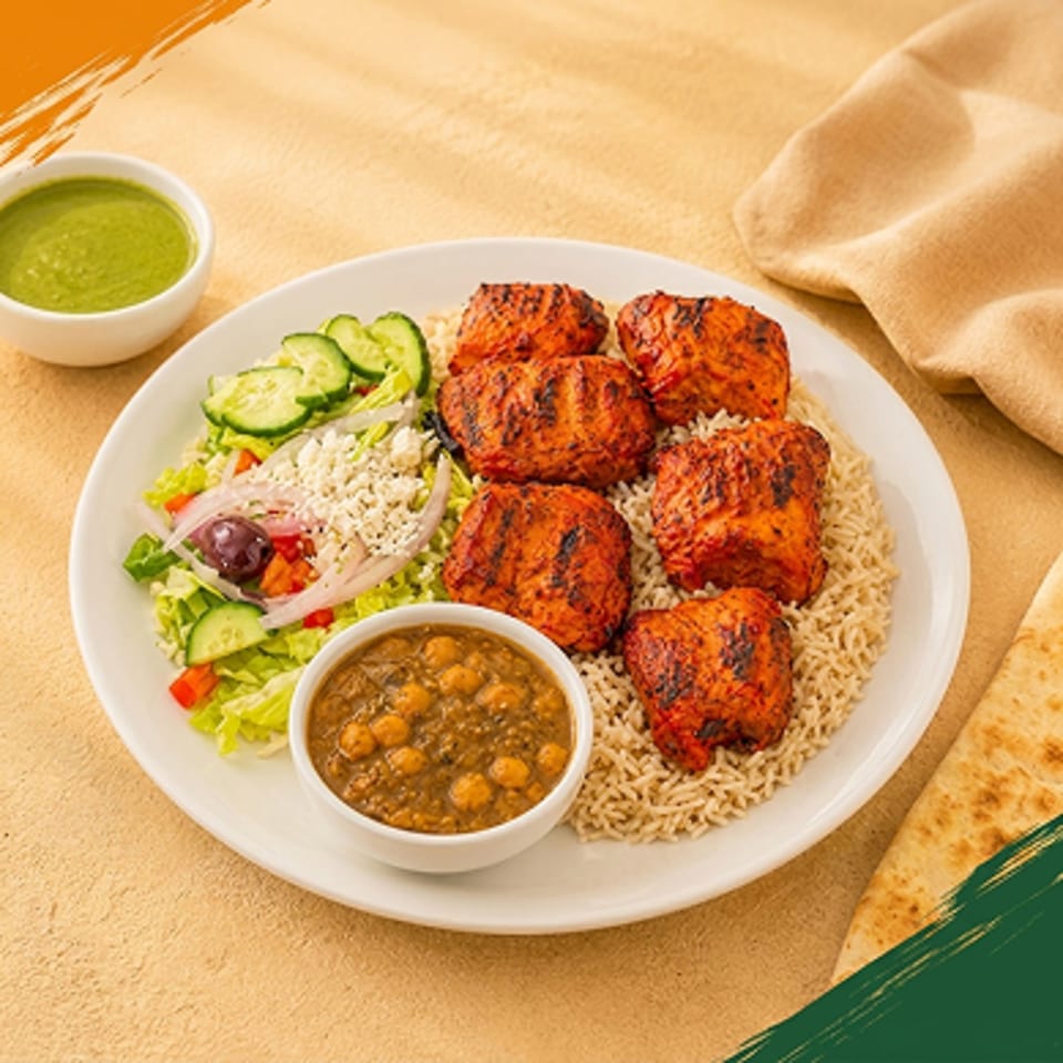 Grilled chicken pieces with rice, salad, chickpea curry, and green sauce on a white plate.