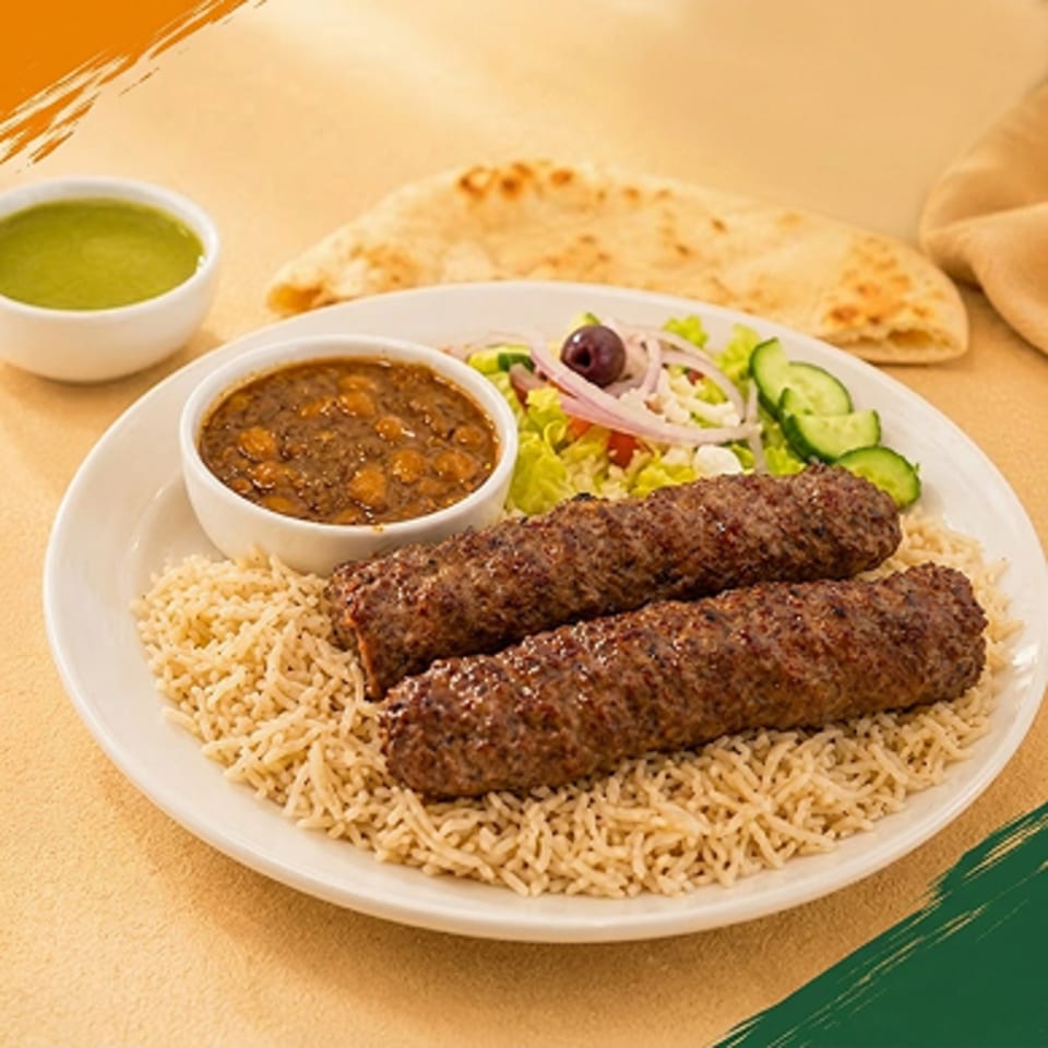 Two seekh kebabs on a bed of rice, with a side of chana masala, salad, and naan.