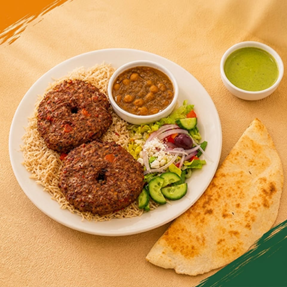 Two round meat patties on rice, with a side of chickpea stew, salad, pita bread, and green sauce.